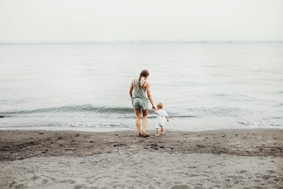白天，女人和婴儿在灰色的沙滩上散步